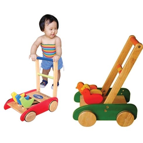 Bé vui vẻ sử dụng xe tập đi con gà bằng gỗ trong không gian rộng rãi, có sự giám sát của người lớn.