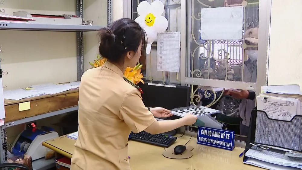 Cán bộ công an đang tiếp nhận và kiểm tra giấy tờ đăng ký xe máy điện của một người dân tại quầy.